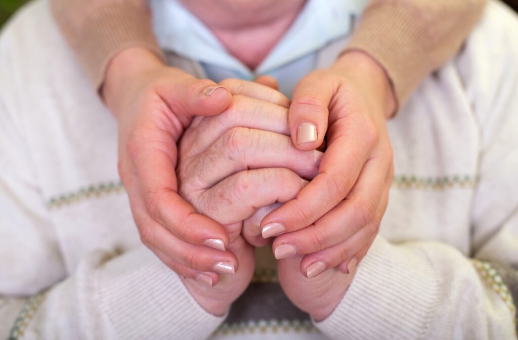A close-up view of a female caregiver's hand's around a seniors hand's in a memory care community