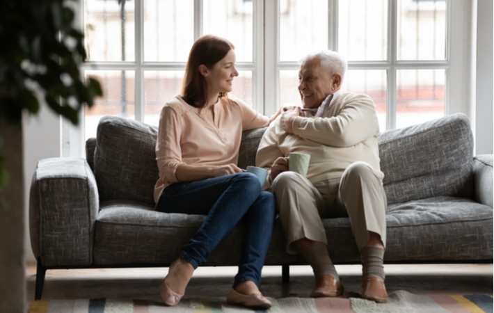A woman speaking with her senior father over coffee on a couch