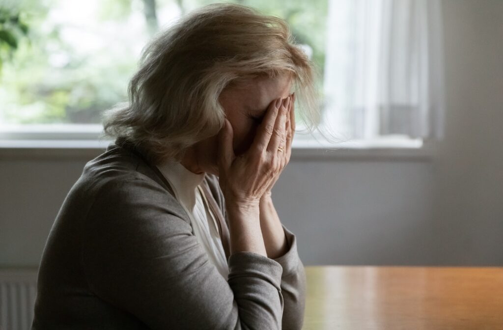 A senior woman sitting at a table with her hands covering her face with grief due to her increasing forgetfulness