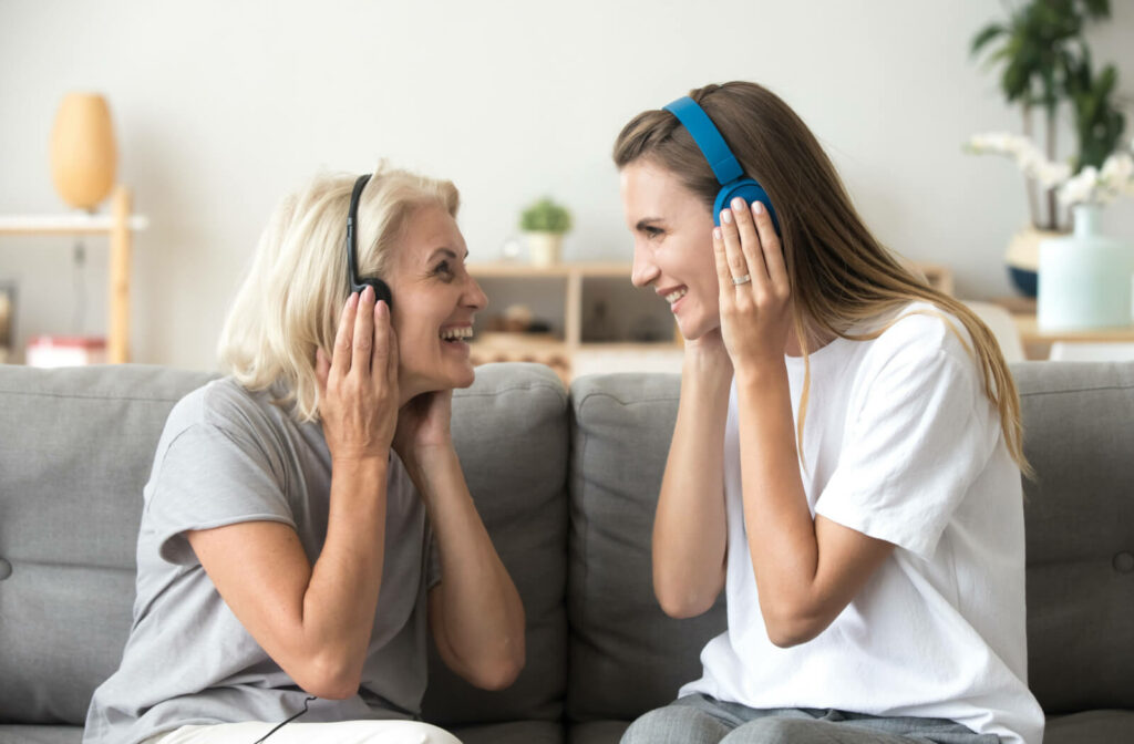 An adult daughter is listening to music on wireless earphones with her mother in memory care.