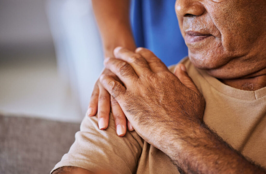 a senior man has his shoulder held by a caregiver in support