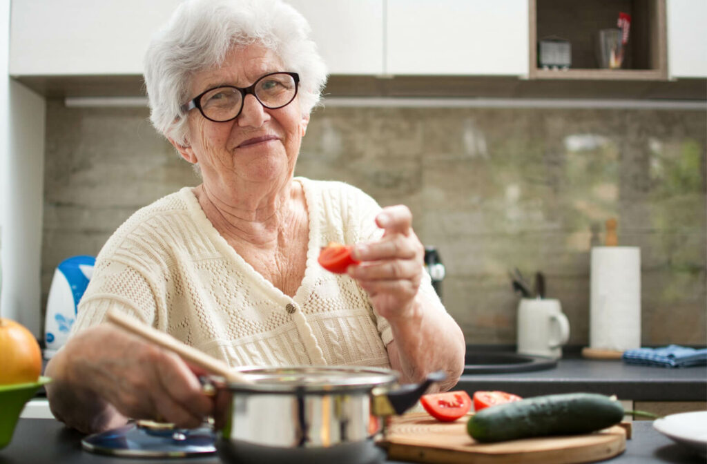 A senior woman with white hair and glasses cooking in a kitchen.